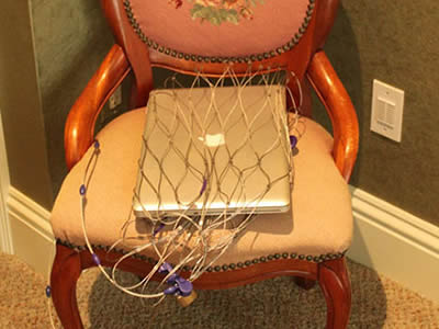 A stainless steel anti-theft backpack protector cable mesh, wrapping a laptop, is placed on a chair.
