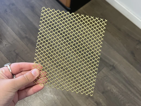 A person holding a brass expanded metal mesh square sample