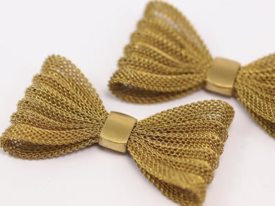 Two brass mesh bow-knots are placed on white paper.