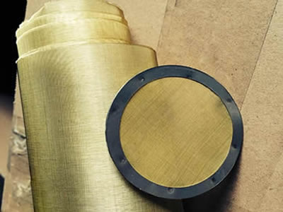 A brass round filter disc with rubber edge beside a roll of brass wire cloth.