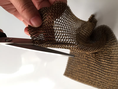 A pair of scissors is cutting the chain braided ring mesh.