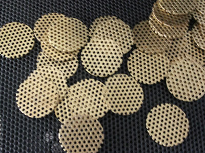 There are many round brass perforated metal discs on black perforated mesh.